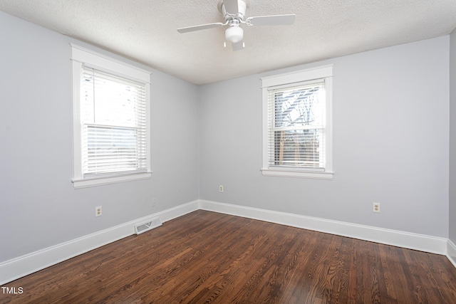 empty room with a textured ceiling, a wealth of natural light, dark wood-style floors, and visible vents