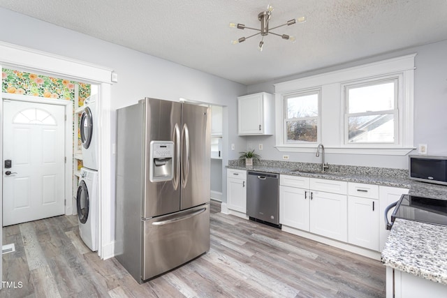 kitchen featuring light wood finished floors, stainless steel appliances, stacked washer / dryer, white cabinets, and a sink