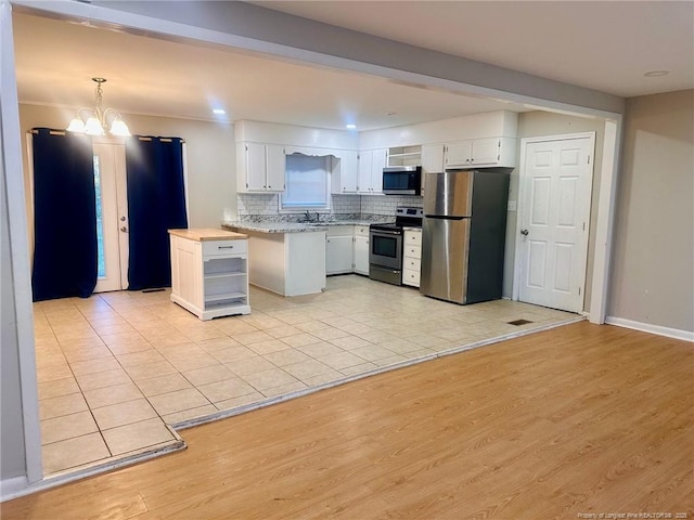 kitchen featuring stainless steel appliances, tasteful backsplash, an inviting chandelier, light wood-style floors, and white cabinets