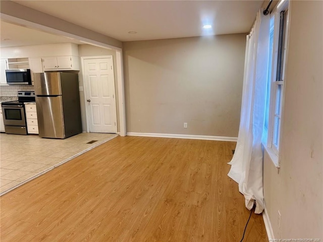 kitchen with baseboards, stainless steel appliances, light wood-type flooring, white cabinetry, and backsplash