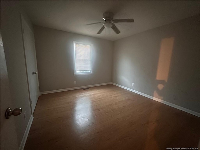 unfurnished room with ceiling fan, visible vents, baseboards, and dark wood-style flooring