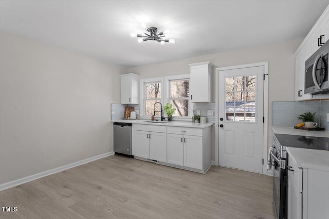 kitchen with stainless steel appliances, sink, white cabinets, and light hardwood / wood-style flooring