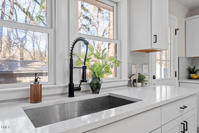 kitchen featuring tasteful backsplash, white cabinetry, light stone countertops, and sink