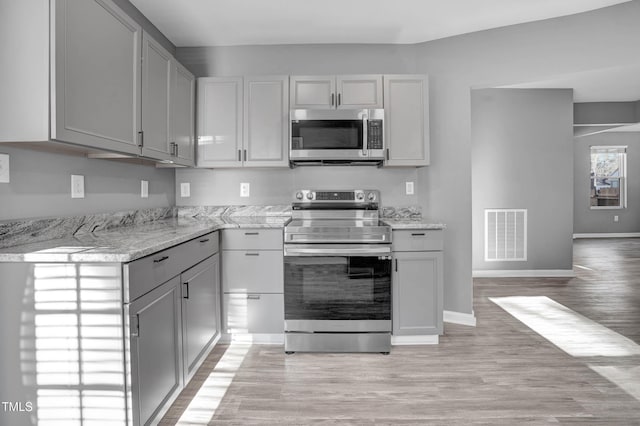 kitchen with light stone countertops, gray cabinets, and stainless steel appliances