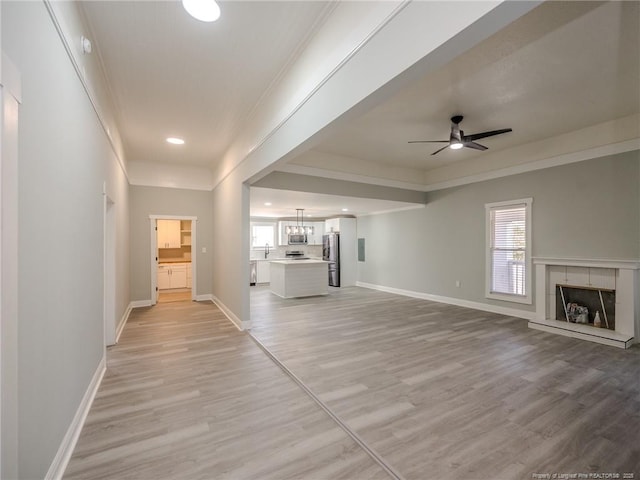 unfurnished living room with light hardwood / wood-style floors, ceiling fan, sink, and a tiled fireplace