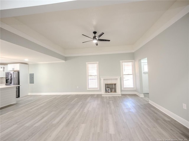 unfurnished living room with light hardwood / wood-style floors, ceiling fan, electric panel, and a tiled fireplace