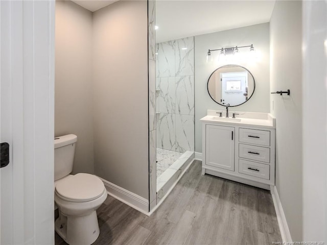 bathroom featuring hardwood / wood-style floors, toilet, tiled shower, and vanity