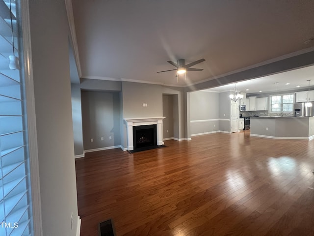 unfurnished living room featuring dark wood-type flooring, ornamental molding, and ceiling fan with notable chandelier