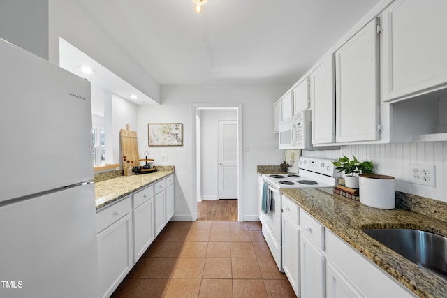 kitchen with white appliances, white cabinetry, sink, stone countertops, and light tile patterned flooring