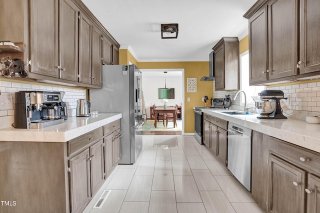 kitchen featuring light stone counters, a sink, ornamental molding, appliances with stainless steel finishes, and backsplash