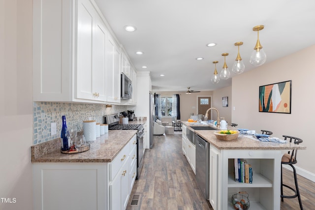 kitchen featuring stainless steel appliances, white cabinetry, hanging light fixtures, and a kitchen breakfast bar