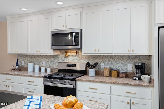 kitchen featuring decorative backsplash, white cabinets, appliances with stainless steel finishes, and light stone countertops