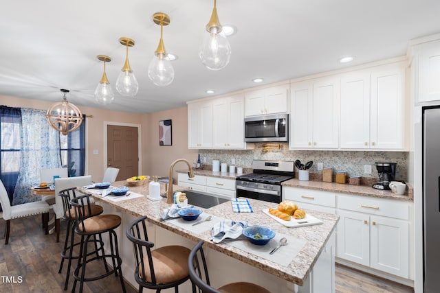 kitchen featuring white cabinetry, pendant lighting, appliances with stainless steel finishes, and a kitchen island with sink