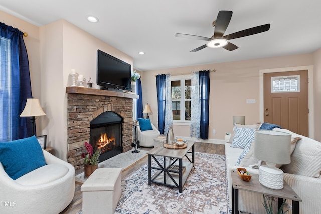 living room featuring ceiling fan, plenty of natural light, a stone fireplace, and light wood-type flooring