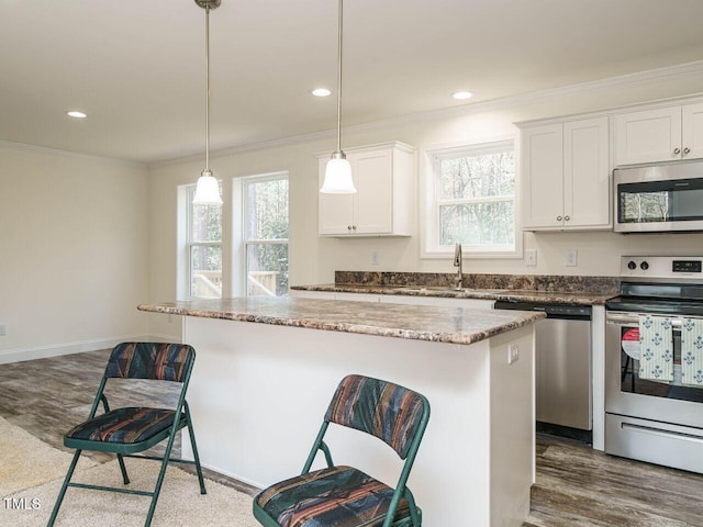 kitchen featuring a center island, hanging light fixtures, appliances with stainless steel finishes, a kitchen breakfast bar, and white cabinets