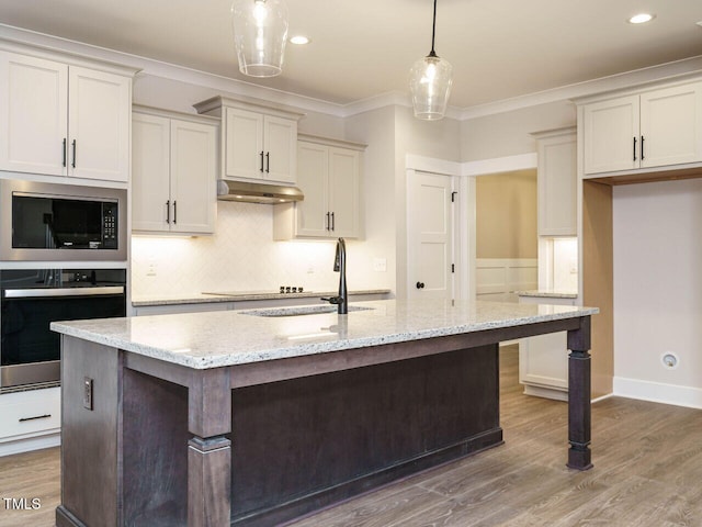 kitchen featuring light stone countertops, an island with sink, built in microwave, decorative light fixtures, and oven