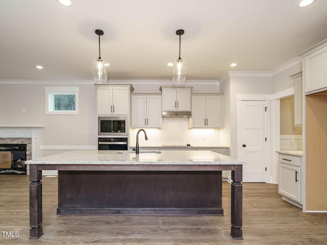 kitchen featuring built in microwave, an island with sink, oven, and light stone counters