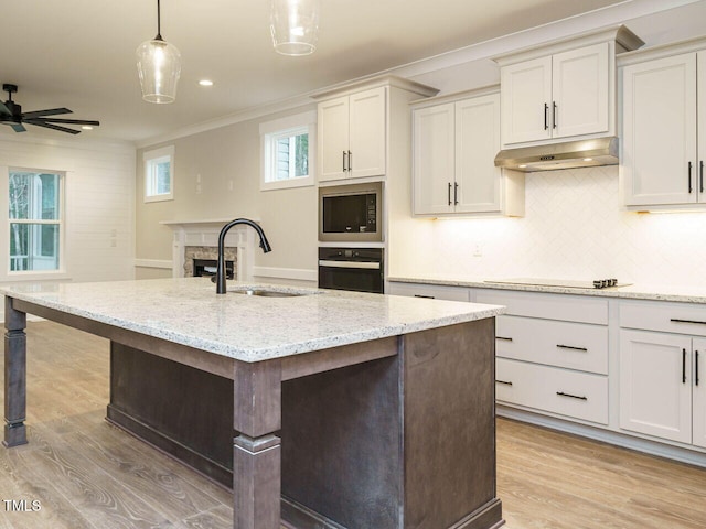 kitchen featuring built in microwave, sink, oven, hanging light fixtures, and a kitchen island with sink