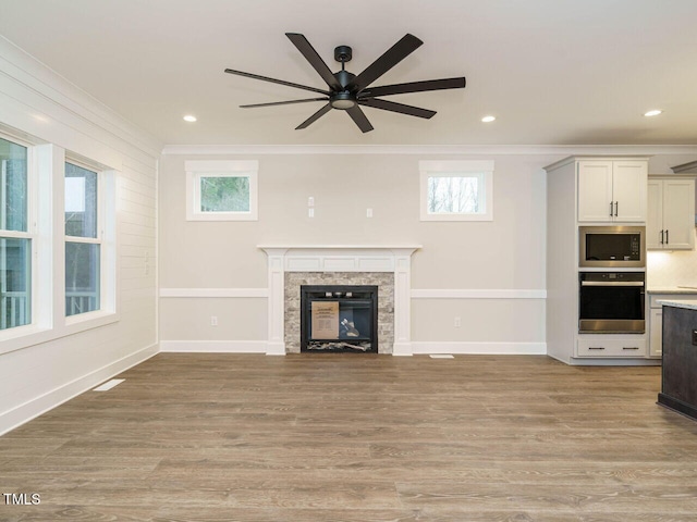 unfurnished living room with a glass covered fireplace, a healthy amount of sunlight, wood finished floors, and ornamental molding