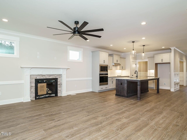 kitchen with built in microwave, crown molding, hanging light fixtures, oven, and a kitchen island with sink