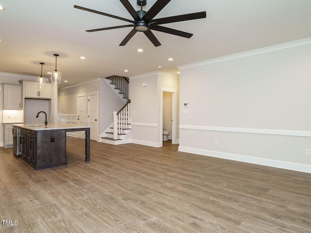 kitchen with light wood finished floors, crown molding, an island with sink, a kitchen breakfast bar, and a sink