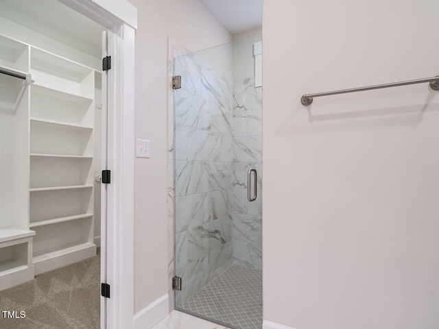 bathroom featuring a walk in closet, baseboards, and a stall shower