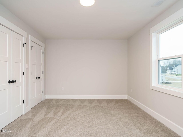 unfurnished bedroom featuring light colored carpet and multiple closets