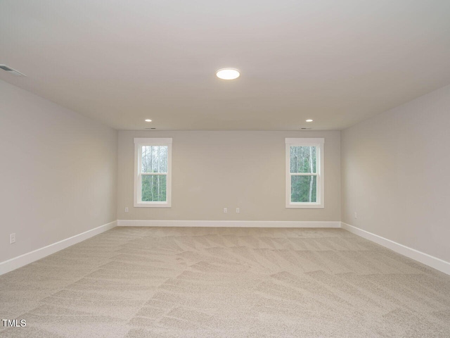 spare room featuring plenty of natural light, light colored carpet, and baseboards