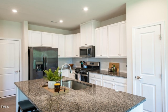 kitchen featuring dark stone countertops, white cabinetry, a kitchen island with sink, and appliances with stainless steel finishes