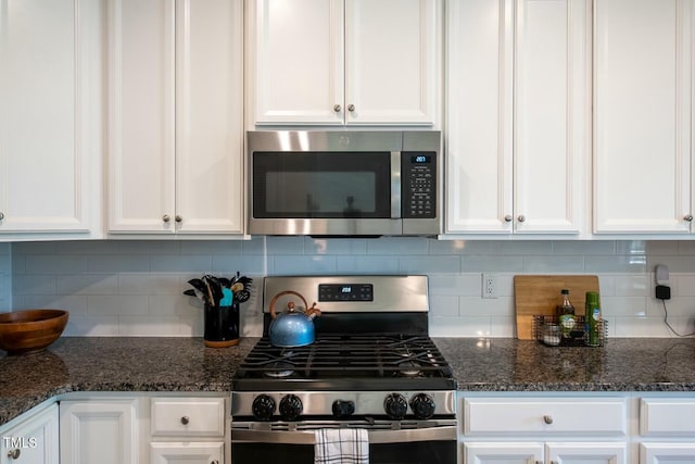 kitchen featuring white cabinets, tasteful backsplash, dark stone counters, and appliances with stainless steel finishes