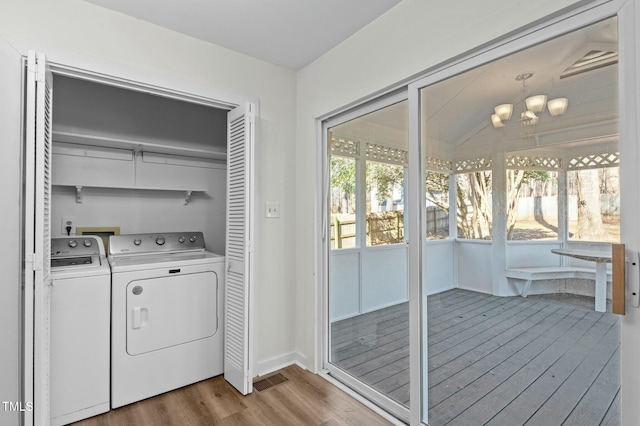 washroom featuring washing machine and clothes dryer, an inviting chandelier, and hardwood / wood-style flooring