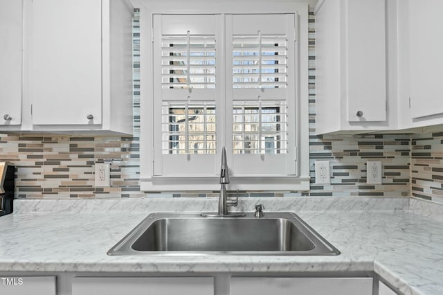 kitchen with a sink, light stone countertops, tasteful backsplash, and white cabinetry