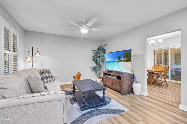 living area featuring ceiling fan with notable chandelier, baseboards, and light wood-style floors