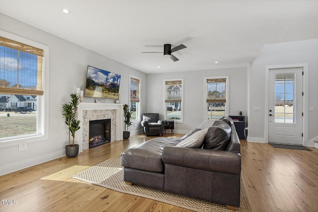 living room with a tiled fireplace, ceiling fan, and light wood-type flooring