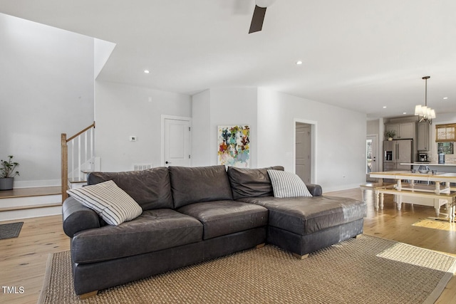 living room with ceiling fan with notable chandelier and light wood-type flooring