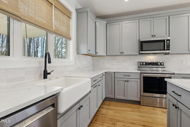 kitchen featuring tasteful backsplash, stainless steel appliances, gray cabinets, and sink