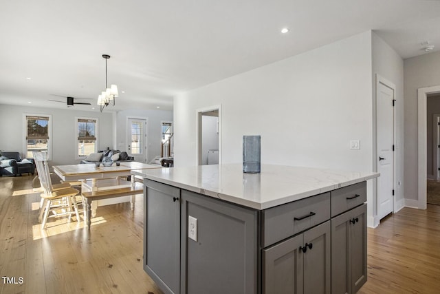 kitchen featuring gray cabinets, a center island, light stone countertops, light hardwood / wood-style floors, and decorative light fixtures