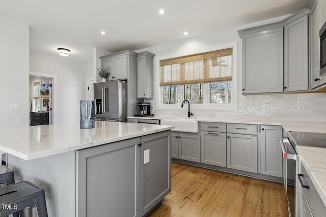 kitchen with sink, light stone counters, light hardwood / wood-style flooring, gray cabinets, and stainless steel appliances