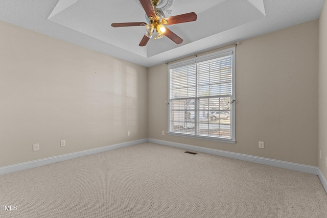 empty room with a tray ceiling, ceiling fan, and carpet flooring