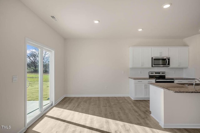 kitchen with backsplash, white cabinets, light wood-type flooring, dark stone counters, and stainless steel appliances