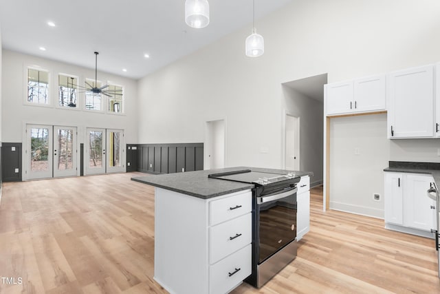 kitchen with stainless steel electric stove, pendant lighting, a towering ceiling, white cabinetry, and light wood-type flooring