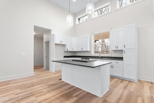 kitchen with light hardwood / wood-style flooring, decorative light fixtures, white cabinets, a towering ceiling, and a center island