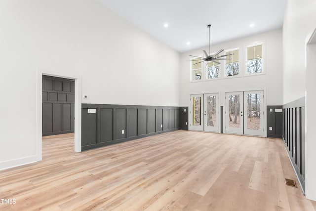 unfurnished living room featuring light wood-type flooring, a towering ceiling, and ceiling fan