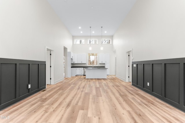 unfurnished living room featuring light hardwood / wood-style floors, a high ceiling, and sink