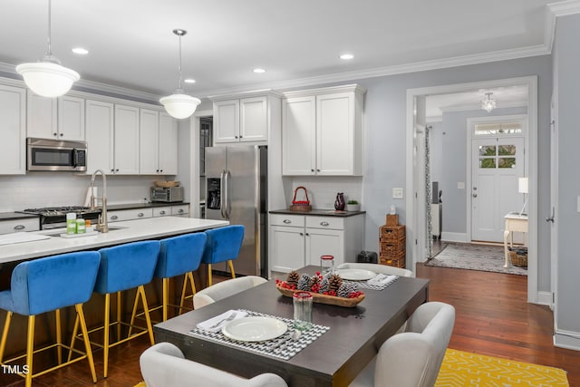 kitchen with appliances with stainless steel finishes, a breakfast bar, white cabinets, hanging light fixtures, and ornamental molding