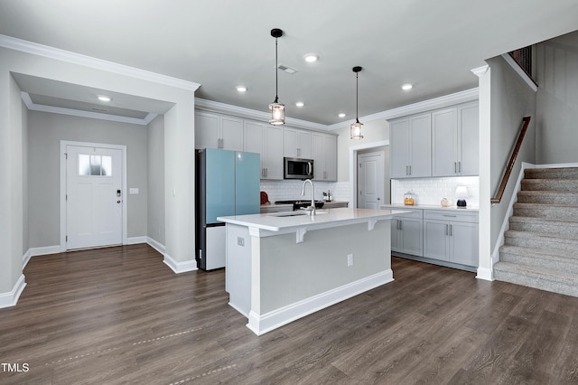 kitchen with gray cabinetry, tasteful backsplash, refrigerator, hanging light fixtures, and an island with sink