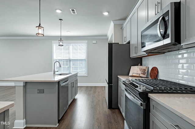 kitchen featuring pendant lighting, gray cabinets, a kitchen island with sink, stainless steel appliances, and ornamental molding