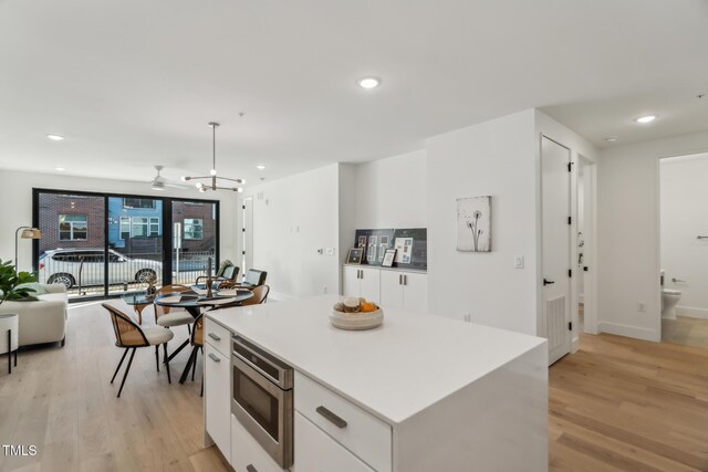 kitchen featuring stainless steel microwave, light wood finished floors, a kitchen island, and white cabinetry