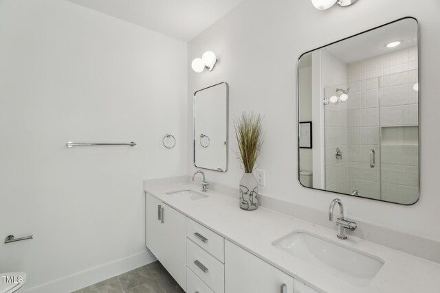 full bathroom featuring a sink, baseboards, a stall shower, and double vanity