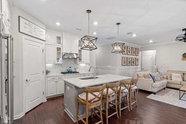 kitchen featuring sink, hanging light fixtures, an island with sink, white cabinets, and a kitchen bar